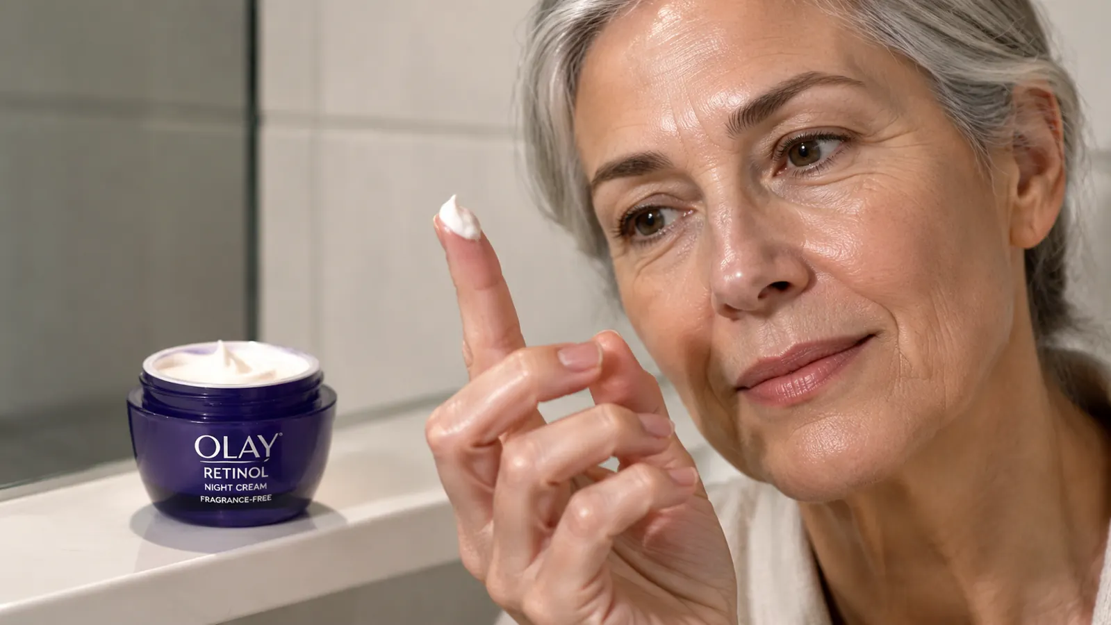 Close-up of a fingertip holding a small amount of Olay night cream next to the open jar
