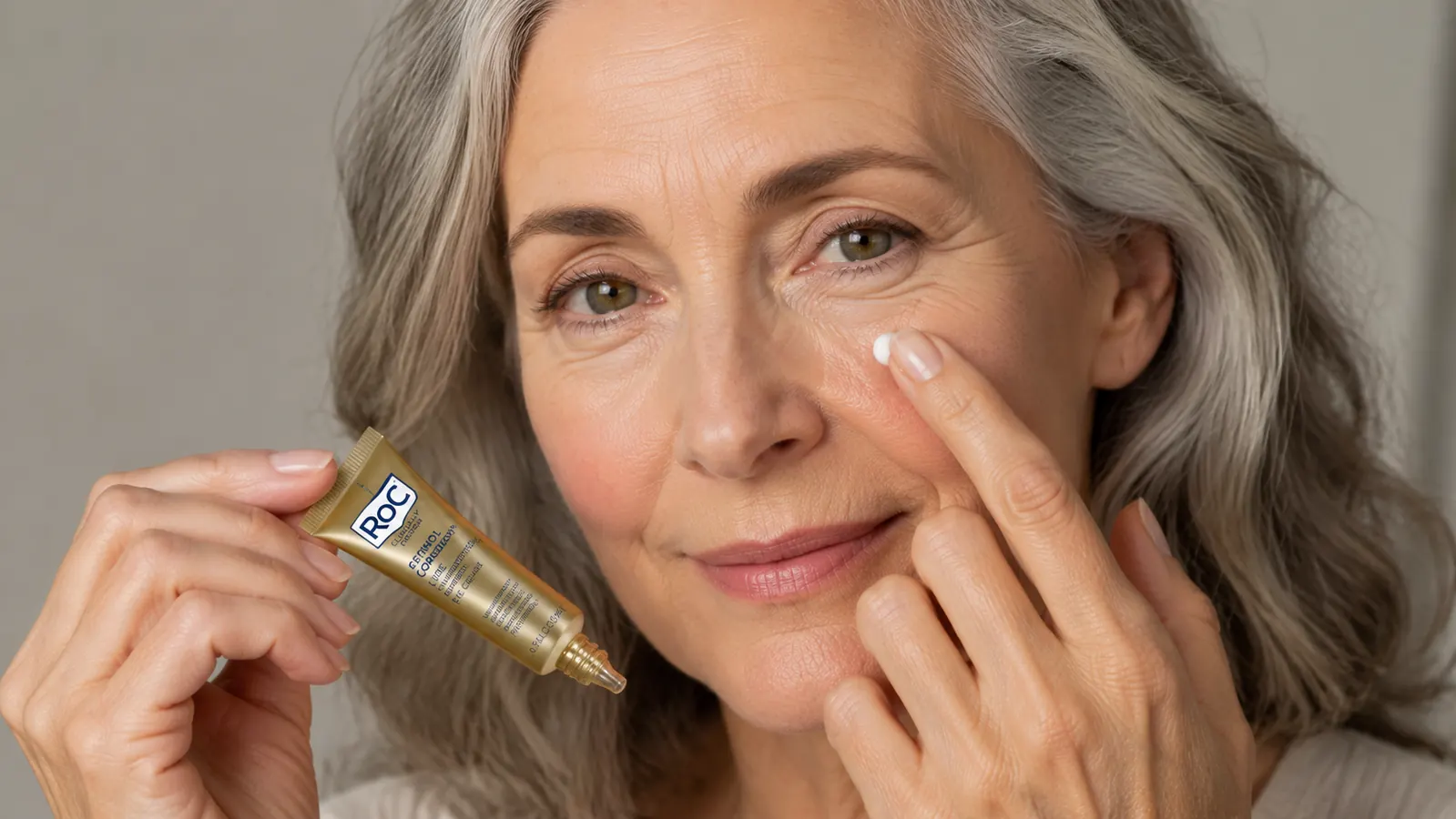 RoC Retinol Correxion Under Eye Cream tube held in a woman's hand near her face, showing the cream's white texture on a fingertip